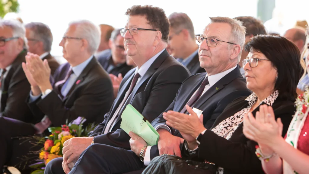 Ein Eventfoto von mehreren Personen, die in einer Reihe sitzen und bei einer Veranstaltung applaudieren.